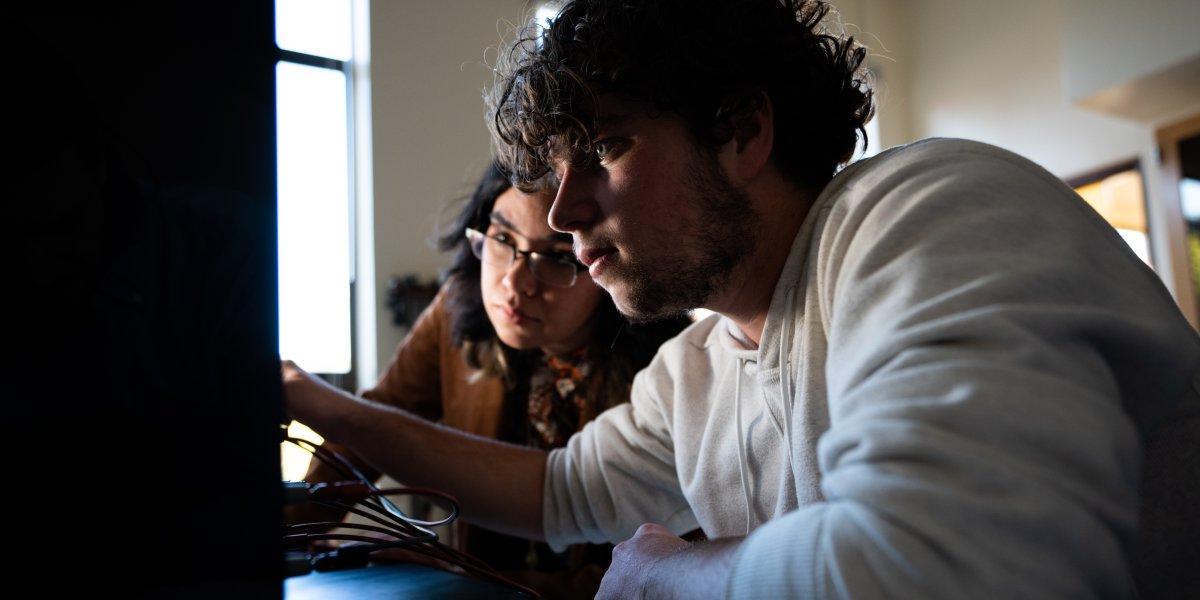 A man and woman look at a computer screen in low lighting